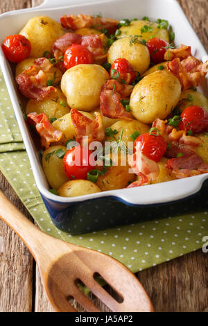 Tasty new potatoes baked with bacon, herbs and tomatoes close-up in a baking dish. Vertical Stock Photo