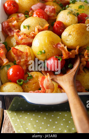 Hot new potatoes baked with bacon and tomatoes close-up in a baking dish. vertical Stock Photo