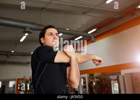 Young sportsman standing indoor and stretching triceps before gym workout. Stock Photo