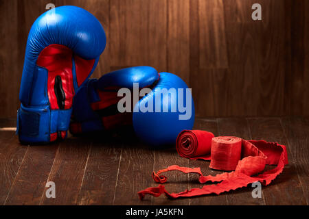 Blue and red boxing gloves with two rolls of hand bandage on wooden background. Stock Photo