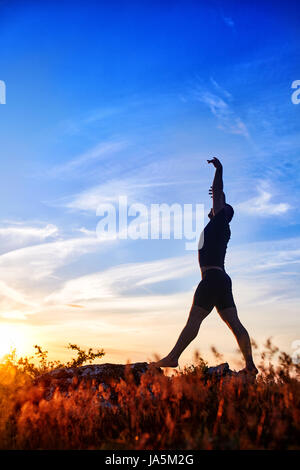 Silhouette of young man doing yoga on the meadow at sunset in the countryside. Stock Photo