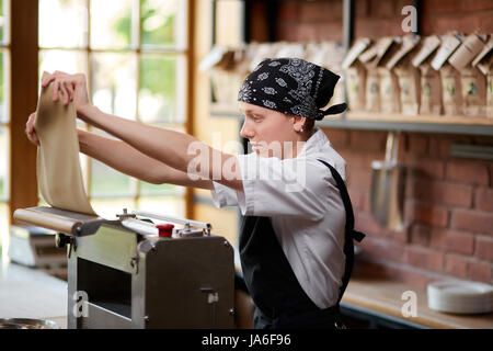 Woman working with dough and pasta rolling machine on the kitchen of restaurant. Making pasta. Making pasta in restaurant. Woman preparing knead for p Stock Photo
