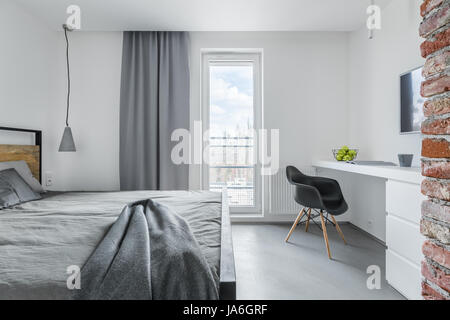White bedroom with brick elements, balcony, double bed, desk and chair Stock Photo