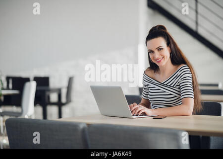 Business lady with positive look and cheerful smile is sitting in a cafe and looking at the camera. Stock Photo