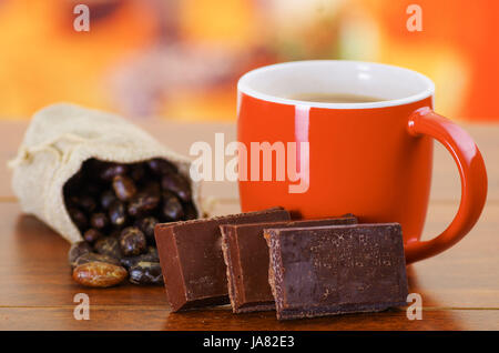 Dry cocoa bean in a small sack and a cup of chocolate over a wooden background Stock Photo