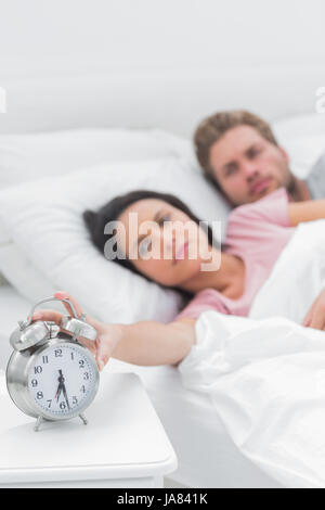 Tired woman turning off the alarm clock while she is in bed with her partner Stock Photo