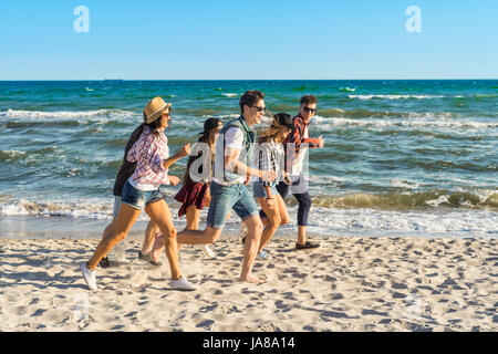 Group of hipster young friends running along beach together Stock Photo