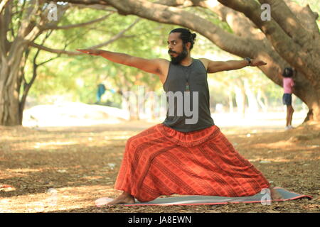 Young man performing the warrior II pose. Veerabhadrasana. Location - Cubbon Park, Bangalore. Stock Photo