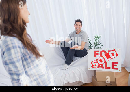 Man in his new house chatting with his wife next to a sign with sold written on it Stock Photo