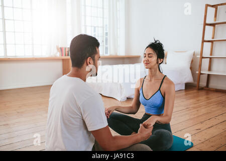Beautiful couple in sitting together holding hands at home and meditating. Young man and woman doing yoga together at home. Stock Photo