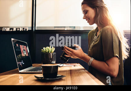 Side view of female vlogger looking at camera while editing video on laptop. Young woman working on her daily vlog. Stock Photo
