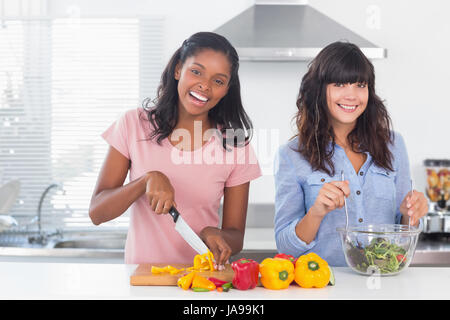 Happy friends preparing a salad together at home in kitchen smiling at camera Stock Photo