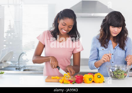 Cheerful friends preparing a salad together at home in kitchen Stock Photo