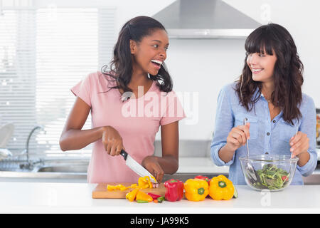 Laughing friends preparing a salad together at home in kitchen Stock Photo