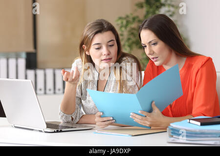 Two serious co-workers commenting a report together on a desk at in an office interior Stock Photo
