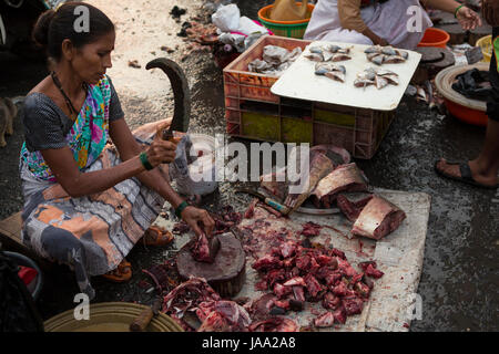 A lady chops up fresh fish on the floor at Sassoon Docks in Mumbai, India. The Sassoon Docks is one of the oldest docks in Mumbai Stock Photo