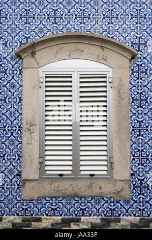 traditional Portuguese tiles on the exterior wall of a building with a window with shutters. Stock Photo