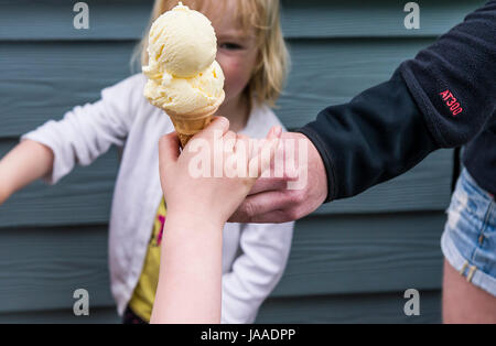 An adult giving an ice cream cone to a child. Stock Photo