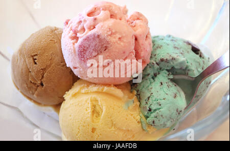 Spoon digging in mint chocolate chip ice cream, one of four scoops of ice cream in a glass bowl Stock Photo