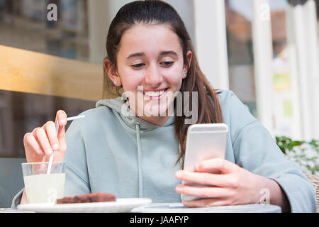 Young Girl At Cafe Reading Text Message On Mobile Phone Stock Photo
