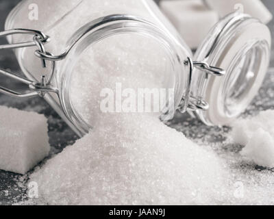 Close up view of white sugar on gray galvanized iron background. Granulated sugar in glass jar and sugar cubes. Sugar background. Copy space. Stock Photo