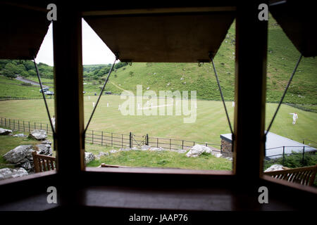 Match play on the pitch a seen through the home team changing room shutters during an annual friendly match between Cravens Cavaliers and Lynton & Lynmouth cricket Club at their ground based inside the Valley of Rocks, North Devon. Stock Photo