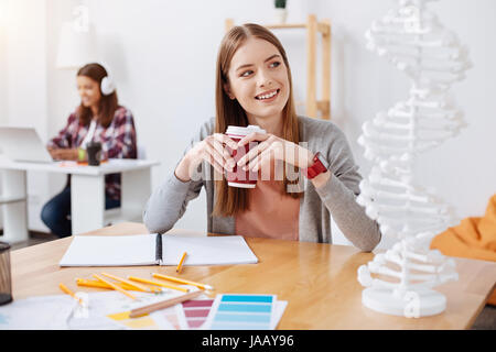 So much to discover. Determined nice wonderful girl sitting at the lecture and examining the model of human DNA while holding a cup of coffee in her h Stock Photo