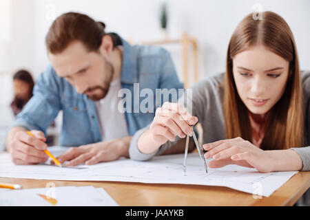 Focused engineers. Lively passionate productive people splitting the project into few task while working on a plan of the new building and drawing som Stock Photo