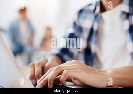 Finding right words. Ambitious attentive active guy sitting at the table and using his computer while working on something important Stock Photo