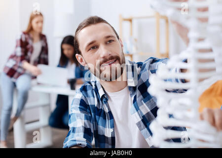 Inspired young scientist. Vibrant engaged clever man examining the model of human DNA while sitting in class and studying genetics Stock Photo