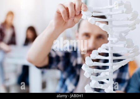 Life in every detail. Handsome attentive smart man using special prototype for studying the structure of DNA while sitting in class Stock Photo