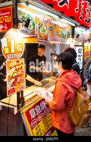 Dotonbori, Osaka. People queuing up to buy traditional Japanese food,  Takoyaki and Okonomiyaki from take-away counter during the evening. Stock Photo