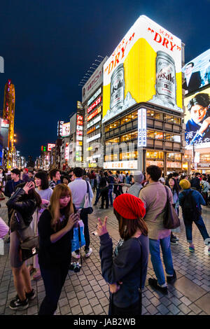 Ebisu bridge in Dotonbori, Osaka. Crowds of tourists enjoying the neon illuminated billboards in the evening, Kanidoraku restaurant with beer can sign. Stock Photo