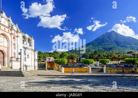 San Juan del Obispo, Guatemala - April 4, 2015: Locals walk in plaza outside one of oldest Catholic churches in Guatemala with Agua volcano behind Stock Photo