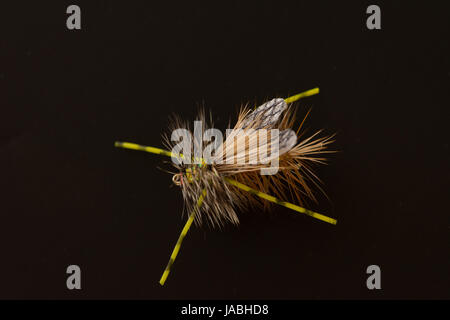 close up of an olive green foam fly fishing fly with white and black foam wings, bristles and antennae against a black background. Stock Photo