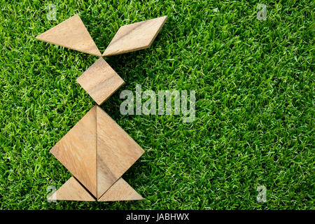 Wooden tangram puzzle in rabbit shape on artificial green grass background (Concept of Happy Easter) Stock Photo