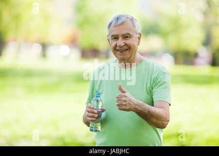 Senior man is drinking water after workout in park. Stock Photo