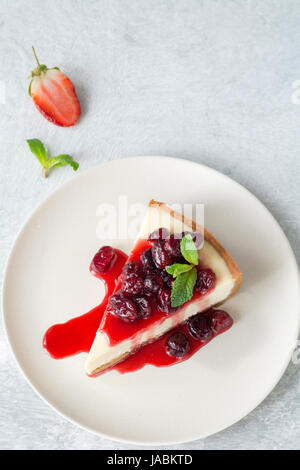 Slice of plain cheesecake with berry sauce decorated with mint leaf on a plate over bright concrete background and copy space. Top view Stock Photo