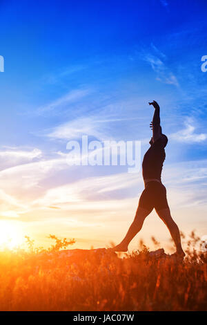Silhouette of young man doing yoga on the meadow at sunset in the countryside. Stock Photo