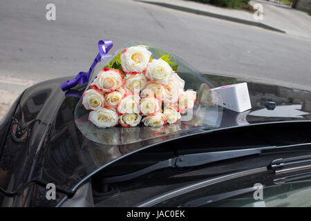 Congratulations to the event. There are a bouquet of roses and wi-fi speaker on the hood of a black car. Stock Photo