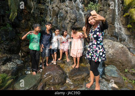 A woman takes a selfie with a group of children at a park in Mandalay, Myanmar (Burma) Stock Photo