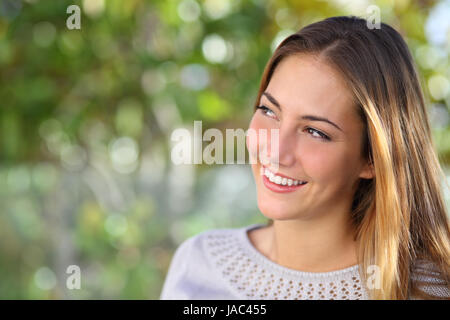 Beautiful pensive woman smiling looking above outdoor with a green unfocused background Stock Photo