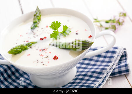 Delicious cream of asparagus soup with green asparagus shoots served in a dainty white bowl on a checkered cloth Stock Photo