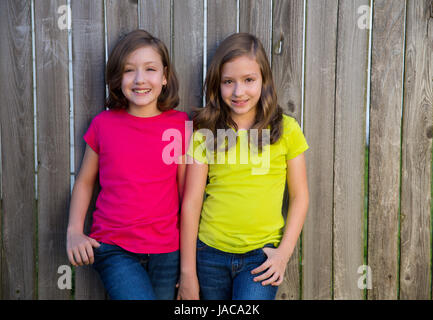 Twin sisters with different hairstyle posing on wood backyard fence Stock Photo