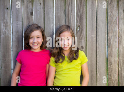 Twin sisters with different hairstyle posing on wood backyard fence Stock Photo