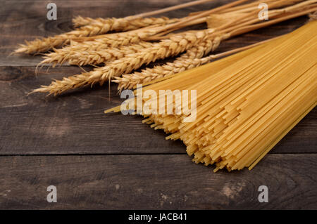 Uncooked pasta and wheat ears on dark wooden background Stock Photo