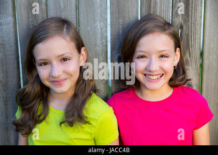 Happy twin sisters with different hairstyle smiling on wood backyard fence Stock Photo