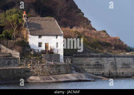 Former coastguard's cottage (whitewashed & with thatched roof) sits above the sea, by the harbour wall & under cliffs - Runswick Bay, England, UK. Stock Photo