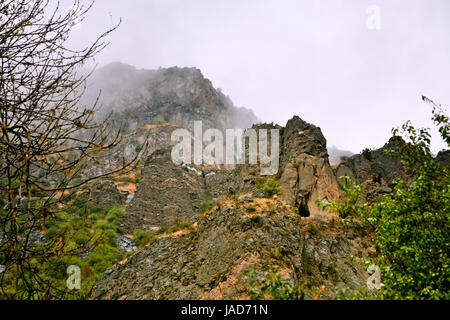 Cliff with cave near Geghard monastery in Armenia in rain. Cliffs surrounding Geghard monastery and Azat river gorge are included together with the monastery in the World Heritage Site listing. Stock Photo