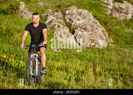Attractive cyclist riding the bike on summer trail near beautiful big rocks. Stock Photo